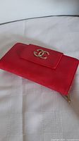 Closed red pigskin wallet showing gold logo on front flap.