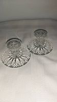Pair of vintage crystal candle holders placed on a white textured cloth surface, showing the full profile of both holders.