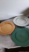 Three plastic picnic platters shown stacked: gold, silver, and sparkly green colors to illustrate color and condition.