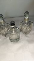 Three vintage stoppered bottles, two square with clear glass stoppers and silver collars, one round with silvered glass stopper and collar.