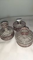 Photo showing three vintage vanity jars made of clear and ruby crystal with intricate cut patterns, placed on a fabric surface.