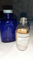 Two medicine bottles: a blue Milk of Magnesia bottle and a clear Listerine bottle with printed label, taken close-up from front.