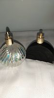 Two vintage perfume bottles side by side on a fabric surface, showing an iridescent ribbed design and a black semi-circular Art Deco style bottle.