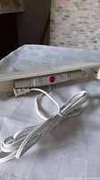 Photo showing the front view of the white under-counter lighting fixture with the red on/off switch and the attached white power cord.