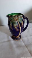 Front view of the pitcher showing gilded palm tree decoration and green interior rim.