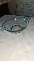 Clear vintage crystal serving dish with deco ornamentation on handles, shown on a white checkered tablecloth from a top angle.