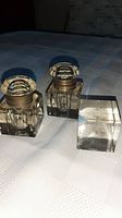 Two clear crystal inkwells with silver-plated and glass tops, and a clear crystal cube paperweight all on a white surface.