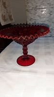 Full view of vintage red glass Fenton pedestal fruit bowl showing height, ruffled edge, and pedestal base.