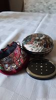 Two items on white cloth: ceramic box with Japanese figures and round make-up mirror in fabric pouch