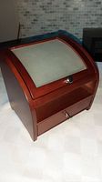 Closed wooden jewelry box with curved glass top showing soft cushioned area beneath and wooden pull drawer with metal knob
