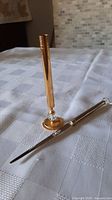 Letter opener with silver handle and gold blade lying on table next to a matching gold holder with crystal decoration.