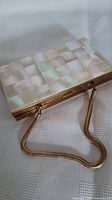 Image showing front side of the rectangular makeup clutch with mother of pearl checkerboard surface and gold-tone metal frame with chain handle.