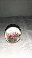 Clear glass vintage paperweight with pink flower inside shown from a side angle on a light fabric surface.