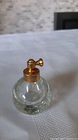 Clear glass vintage perfume bottle showing rounded body and gold spray top under different lighting.