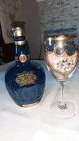 Blue Royal Salute 21 Year Old Scotch Whisky porcelain flask next to a handpainted and gilded wineglass with floral design