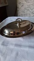 Silverplate serving dish closed with lid on, reflecting light and showing the ring handle on lid.