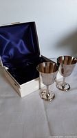 Pair of vintage silverplated goblets standing next to an open satin lined box with blue interior lining.