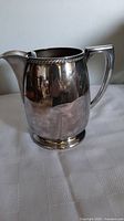 Front and side views of a vintage silverplated jug showing its shape, handle, spout, and decorative rim detail.