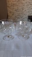 Pair of Waterford Crystal Lismore brandy snifters on a white textured cloth with a neutral tiled background.