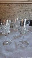 Photo shows three large Waterford crystal wine glasses on a white cloth. One is the Lismore pattern with detailed diamond and star cuts. The other two glasses have the Alana vertical cut design.