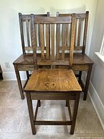 Three brown wooden bar stool chairs stacked closely, showing front view and seat tops.