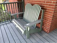 Side view of the vintage Muskoka style outdoor love seat on a porch, showing light green paint and wood with signs of outdoor wear.
