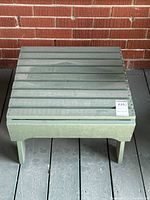 Front view of the light green wooden Adirondack style side table with slatted top showing minor wear and dimensions tag attached.