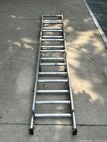 Full view of aluminium extension ladder laid out on pavement, showing overall length and condition.