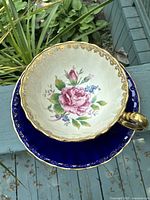 Top-down view of cup inside saucer showing central rose motif and gold trim.