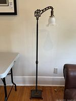 Full view of the tall vintage metal floor lamp with a frosted glass ruffled shade lit from the arm.
