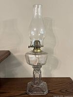 Full view of the assembled antique kerosene oil lamp showing the tall glass chimney, brass burner, and pressed glass base and reservoir.