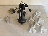 Top down view of disassembled antique style ceiling lamp fixture with 8 metal floral arms, mounting plate, 8 frosted tulip-shaped glass shades, and several incandescent bulbs.