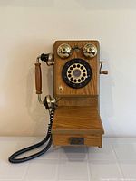 Front view of the antique style oak wall telephone showing the rotary dial, brass bells, and handset with wooden accents.