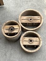Top view of three circular wooden pulley wheels showing wood grain, metal hardware, and keyhole-shaped spindle holes.