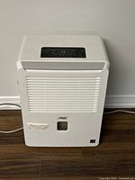 Front view of white Arctic King dehumidifier with air intake grille and water level window.