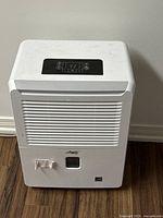 Front view of a white Arctic King compact dehumidifier showing front air vents, water collection area, and brand logo