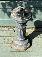Front view of cast cement garden sundial on deck showing overall shape, fluted column base, and rabbit on dial.