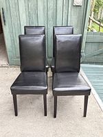Front view of four black faux leather dining chairs arranged in two rows showing the padded backrest and seat with condition details.