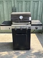 Full front view of the black Cuisinart gas barbecue grill showing the hood with logo and temperature gauge, three burner control knobs, and side burner on the right side.