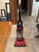Front view of red Dirt Devil Prime Rewind vacuum cleaner showing upright handle, clear dust canister, power control dial, and base with brush roll.
