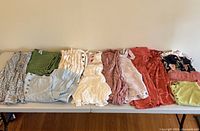 Collection of girls summer clothing items laid out in a row including dresses, tops, and shorts in various colors and patterns.