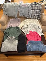 Full view of clothing pieces arranged on furniture, showing various sweaters, tops, pants, and denim overall shorts.