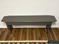 Front view of grey painted wood bench showing smooth top and curved legs.