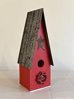 Front-side angle view of red handmade wooden birdhouse with tall galvanized metal roof, star decoration above entrance hole, and red valve handle decoration below.
