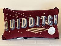 Front view of the burgundy pillow with large embroidered QUIDDITCH letters, golden snitch, and stars.
