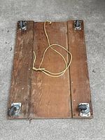 Top view of wooden moving dolly showing four swivel casters mounted at corners and attached rope handle.