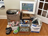 Three boxes containing various kitchen items including glasses, mugs, utensils, an electric kettle, a hand blender, and other miscellaneous kitchen tools