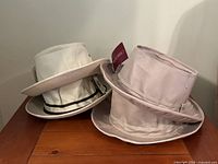 Four beige airflow bucket hats made of cotton with tags on a wooden surface