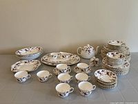 Full set display showing stacked plates, cups, platters, teapot, creamer, and salt and pepper shakers.