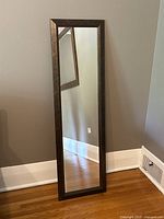 Full view of modern style full length mirror leaning against wall on hardwood floor